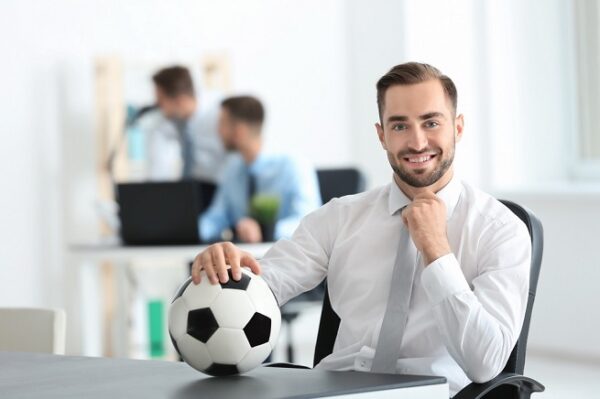 Young handsome man with soccer ball in office